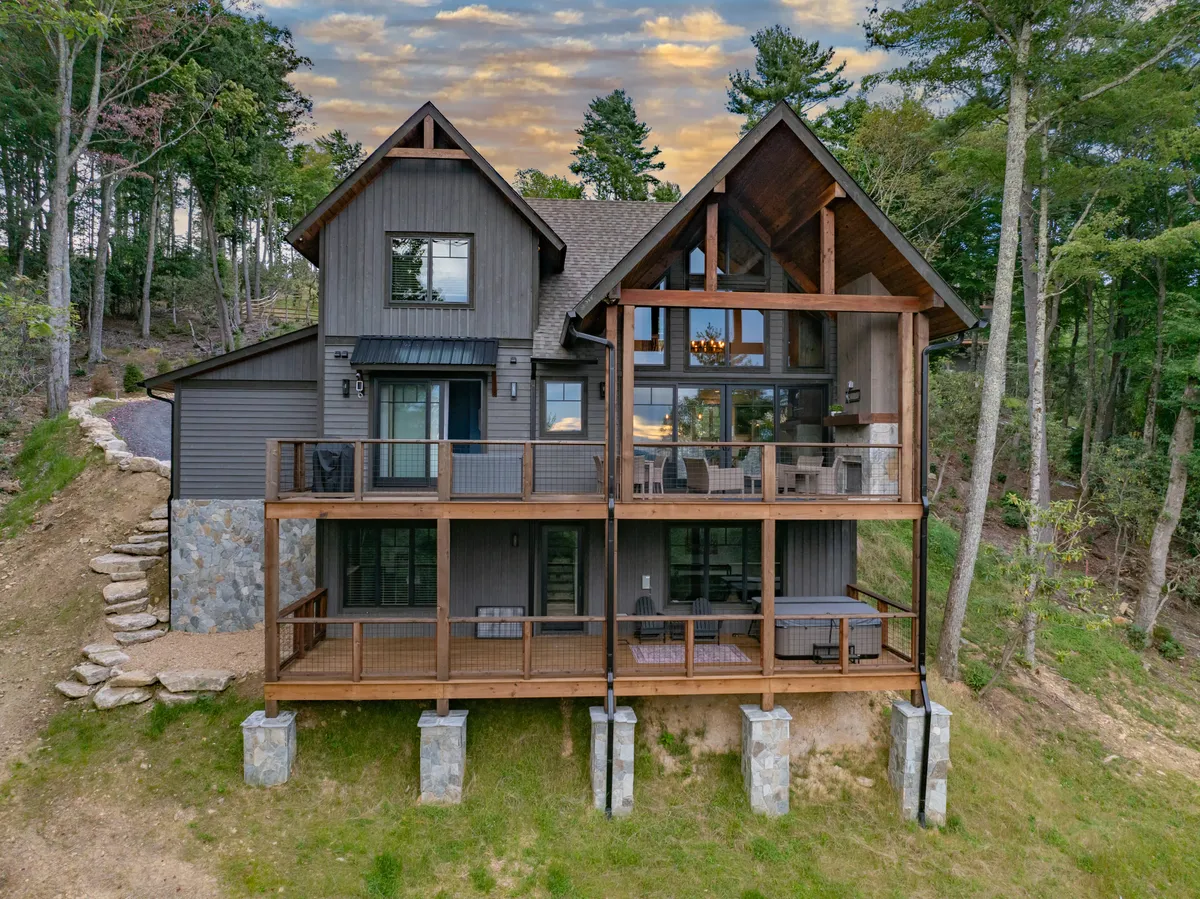 A large wooden deck extends from the home, surrounded by trees and featuring expansive windows that bring the outdoors in. The deck offers space for outdoor dining or enjoying nature, with a cozy, serene atmosphere that invites relaxation and work breaks alike.