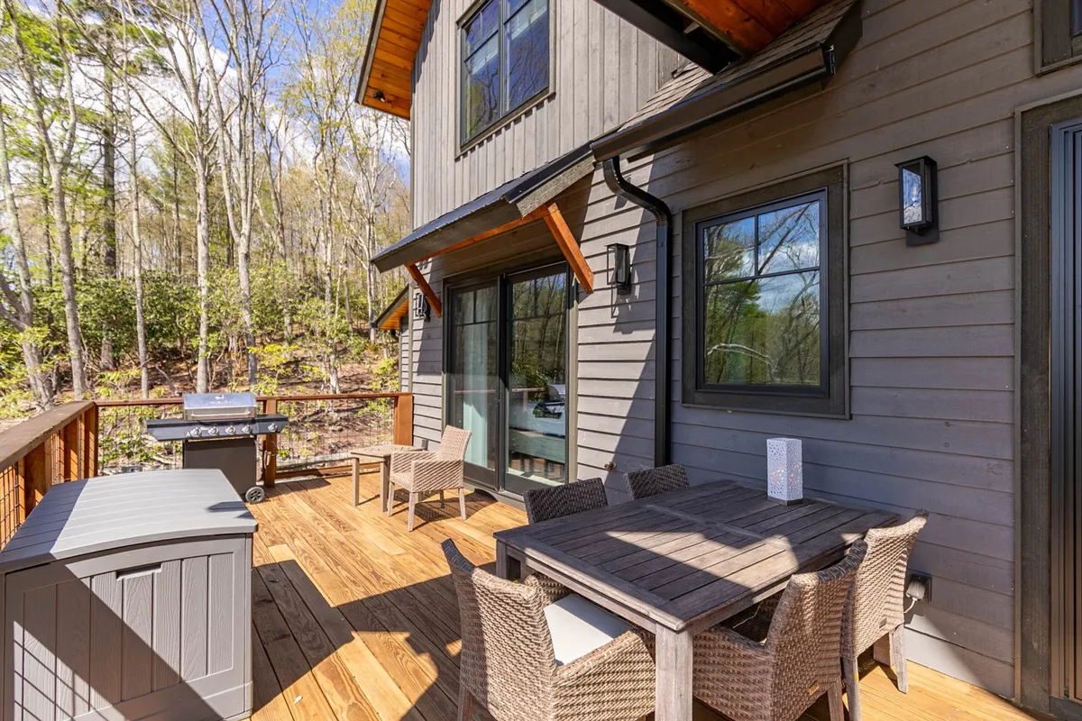 A cheerful outdoor dining setup on a wooden deck with a dining table, chairs, grill, and views of lush nature. The scene suggests ample space for both people and pets to gather, eat, and enjoy the outdoors, echoing the section’s mention of spacious decks and outdoor areas.