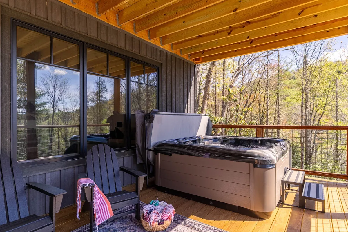 This exterior image features a private hot tub set on a wooden deck, surrounded by Adirondack chairs and lush natural scenery. The tranquil setting is perfect for relaxing while taking in the beauty of the outdoors.