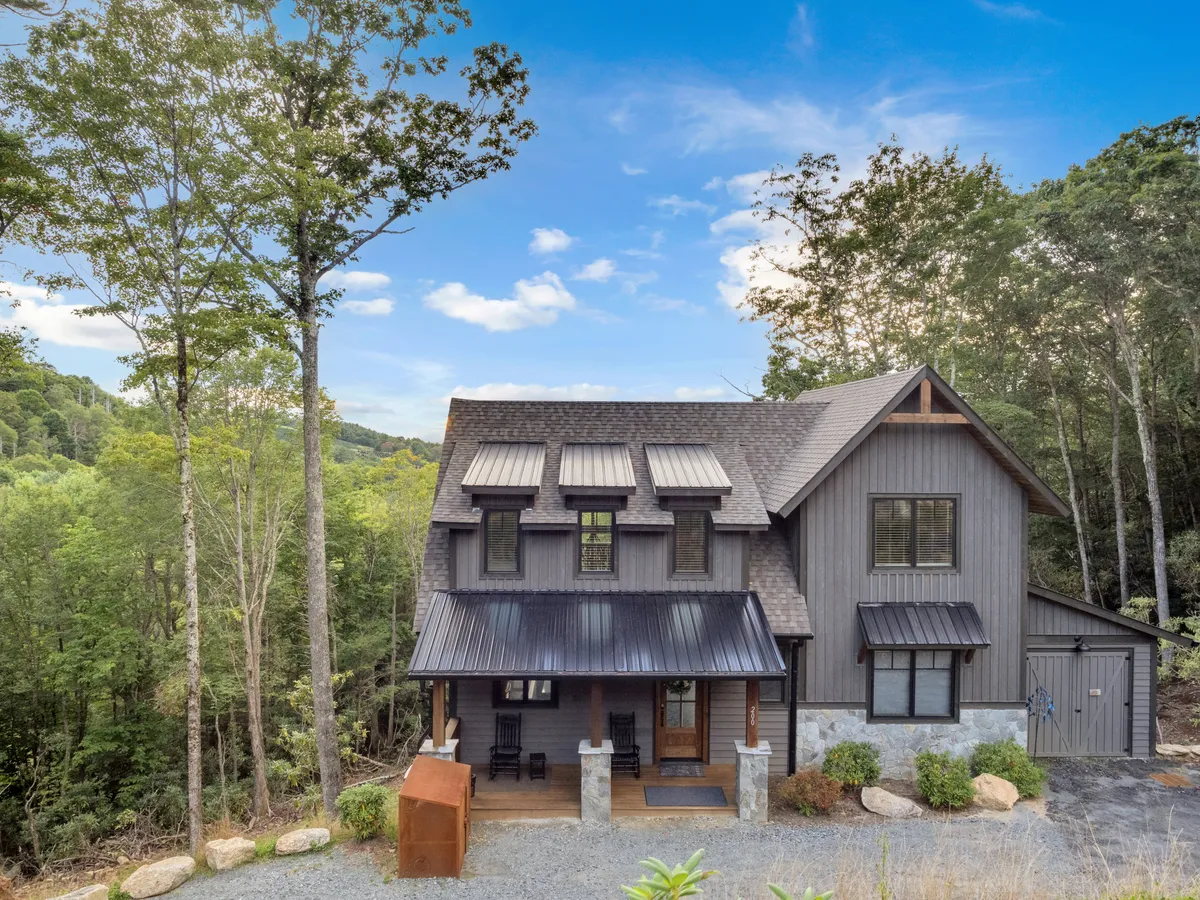A charming front porch with classic rockers sits amid tall trees and serene natural surroundings. The modern architecture is welcoming, and the porch offers a peaceful place to relax, enjoy morning coffee, or watch family members return from nearby trails. The setting seamlessly blends home comfort with the outdoors.