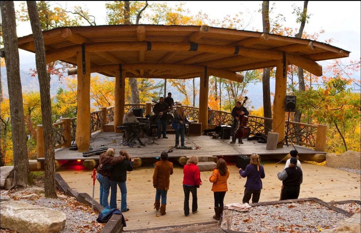 The image shows musicians performing live on an outdoor stage, with families and friends enjoying the show amidst a natural setting. The audience is engaged, and the setting is cheerful, reflecting the amphitheater and lively event offerings at Eagles Nest.