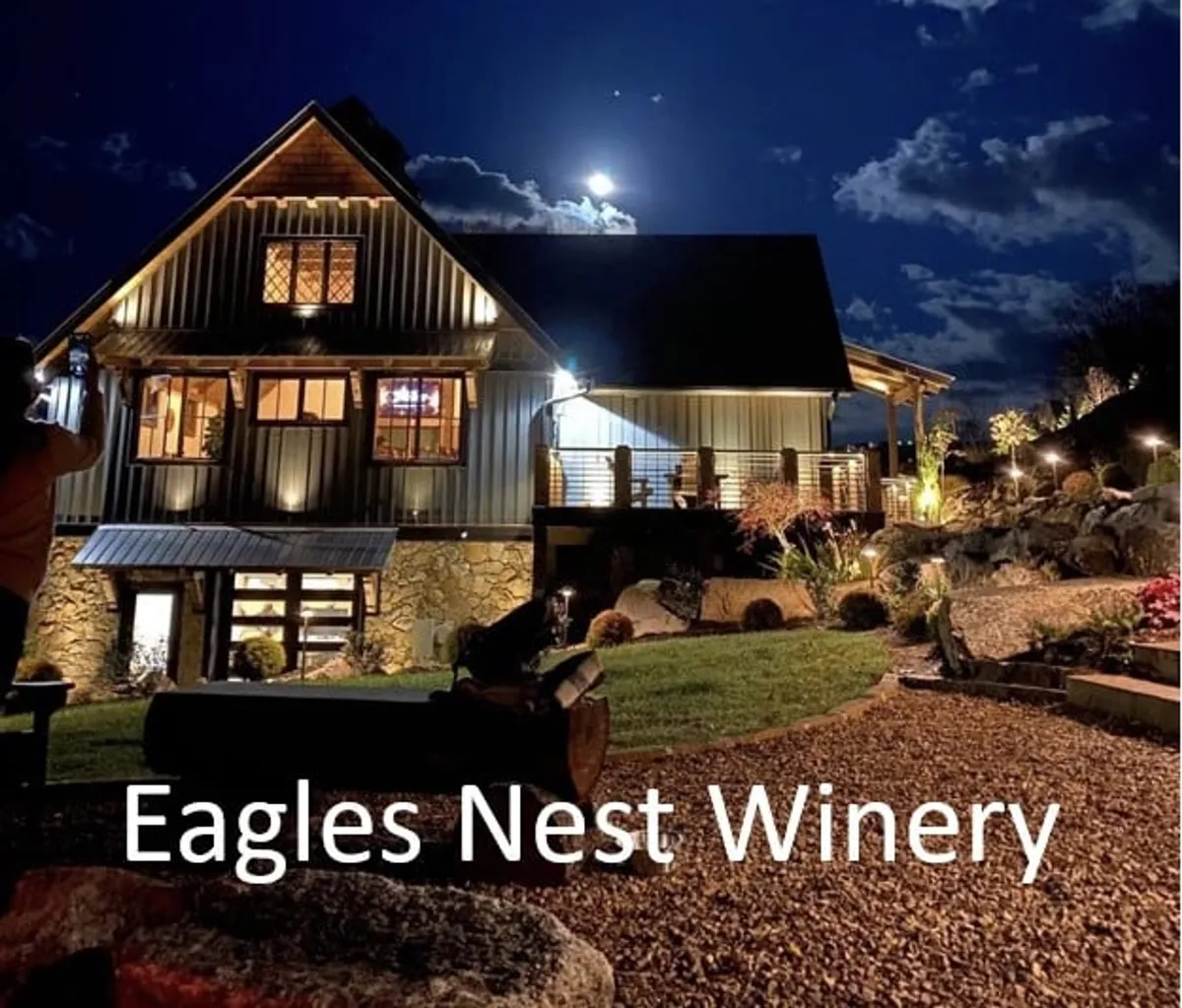 An inviting exterior scene at the community vineyard and winery, featuring a landscaped garden, outdoor seating, and the winery building under the moonlit sky. The relaxed setting hints at evening events, wine tastings, and social gatherings unique to the Eagles Nest community.