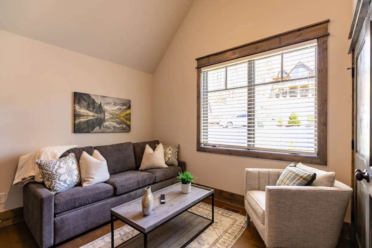 A comfortable interior lounge area featuring a sofa, accent chair, coffee table, and a window offering natural light. The space feels inviting for both work and relaxation, suggesting flexibility in how the area can be used throughout the day.