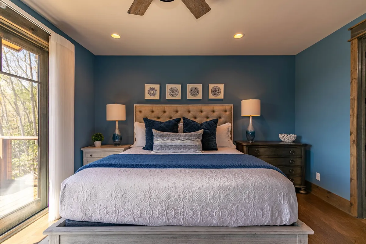 A serene bedroom featuring a king-sized bed with decorative pillows, blue wall art, and soft bedside lighting. The space is inviting, peaceful, and designed for relaxation.