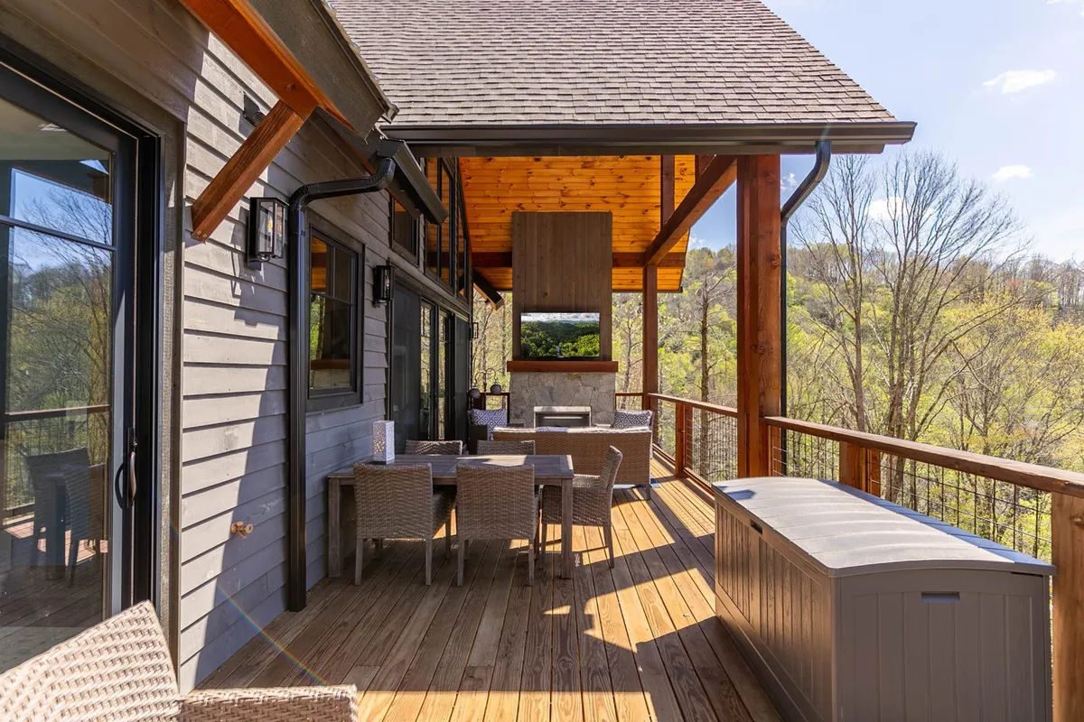 A covered outdoor deck with a dining table and chairs, outdoor fireplace, and beautiful natural landscape in the background. The space is designed for al fresco dining and evening gatherings, blending comfort with the beauty of the outdoors.
