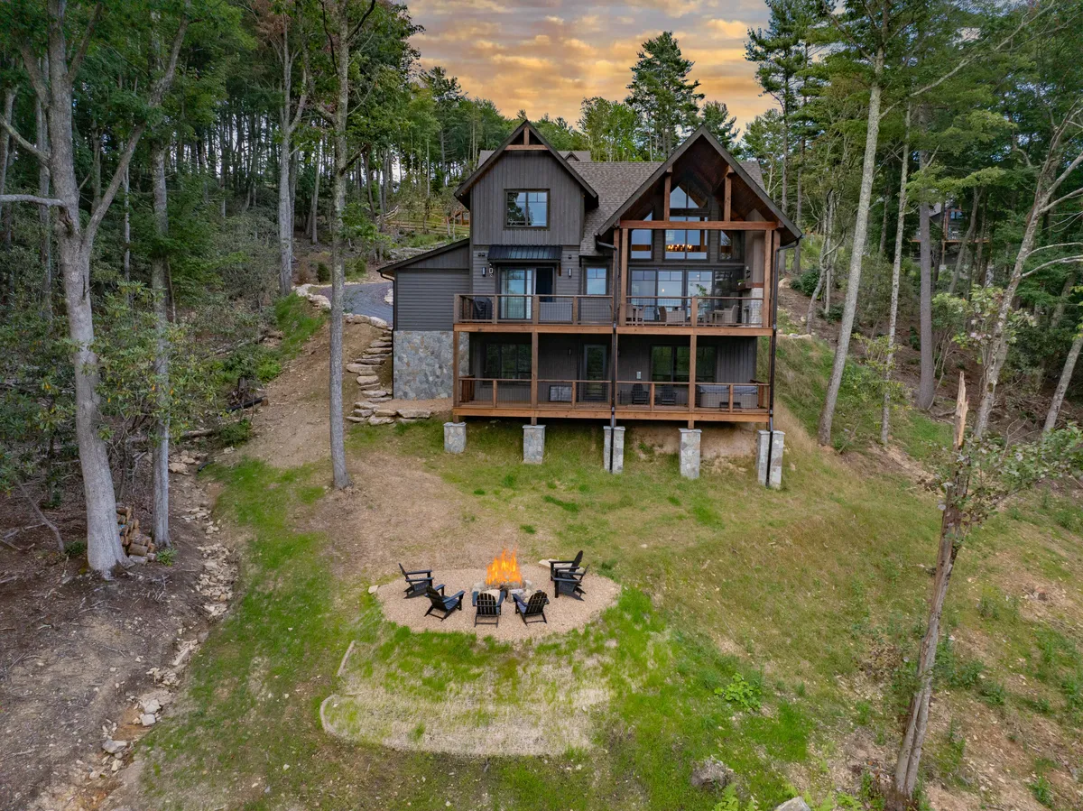 A cozy outdoor fire pit surrounded by Adirondack chairs, nestled among trees just outside the house. The welcoming scene is set for gatherings, marshmallow roasting, and laughter on cool evenings.