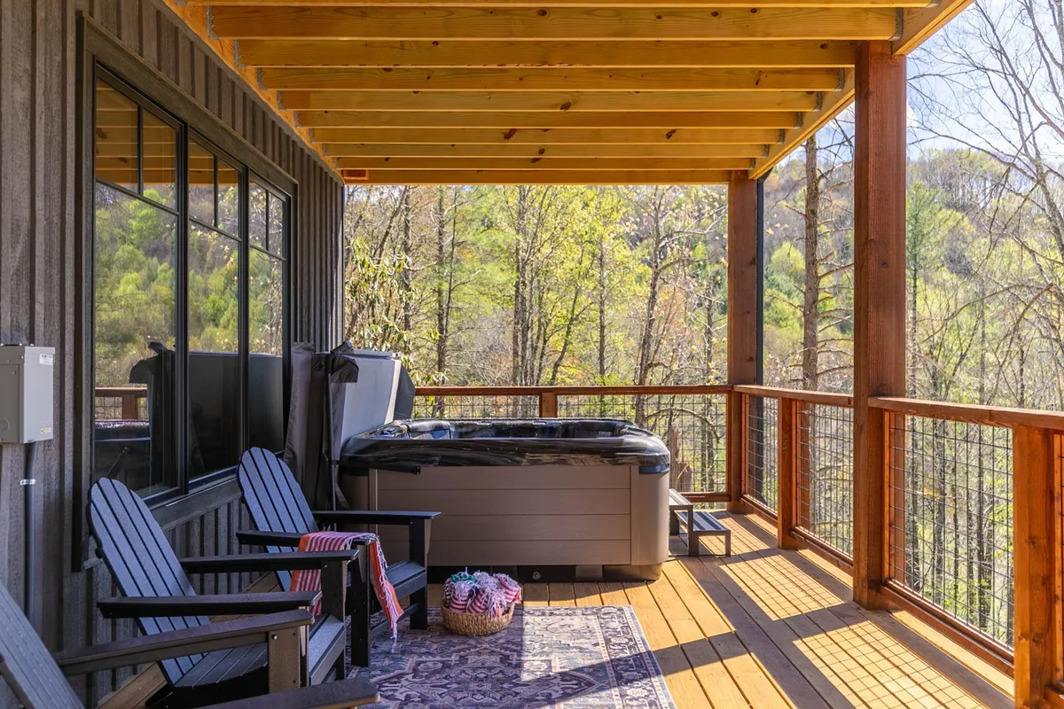 An inviting outdoor deck complete with a brand-new hot tub, rocking chairs, and an area rug set against surrounding greenery. The setting exudes relaxation and offers views ideal for stargazing or unwinding post-adventure.